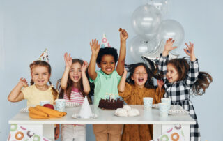 Sits by the table. Children on celebrating birthday party indoors have fun together